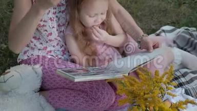 一对幸福的母女在相册里看照片读一本书。 一家人在城市公园野餐，在温暖的晚上。
